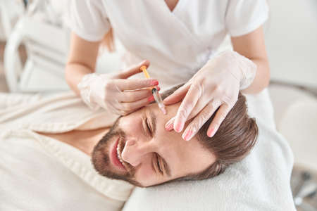 Close up makes mesotherapy injections to young man. Treatment of male by a beautician for tightening and smoothing wrinkles on the face skinの写真素材