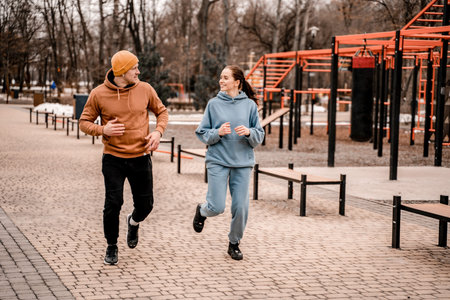 Young man and woman running on street sports ground. Cute couple in sports outfit doing morning...
