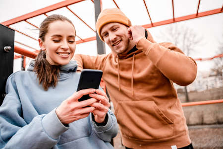 Young attractive sport woman and man in sportswear are smiling and she is holding phone at sports parkの写真素材