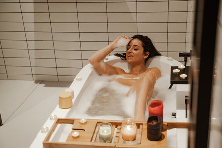 Young and sexy woman relaxing in the cosy bath full of foam and decorated with candles. Healthy...