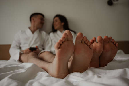 Close up of legs happy young couple in white bathrobes in bed at homeの写真素材