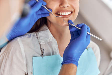 Cheerful positive dentist and client in dentistry. Female patient at dental procedure, doctor using dental instruments in modern dental clinic, close up.の写真素材