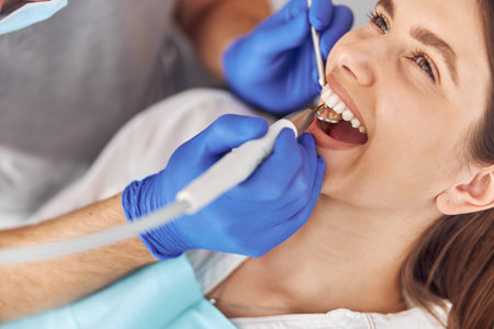 Pretty woman sitting in dental chair while professional doctor fixing her teeth