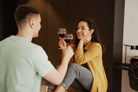 Lovely couple with glasses of wine has romantic dinner at home. Happy young family moved to new apartmentの写真素材