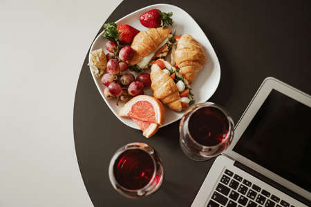 Close up plate of croissant, strawberry and fruits with red wine and laptop. Happy family moving to new apartmentの写真素材