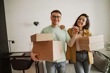 Happy couple holding keys of new apartment with boxes. Young family moving to new apartmentの写真素材