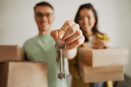 Close up happy couple holding keys of new apartment with boxes. Young family moving to new apartmentの写真素材