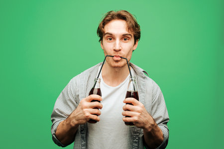 Man holds glass bottles and drinks from two straws, isolated on green backgroundの写真素材