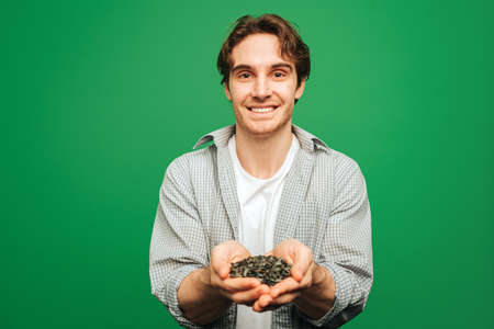 Young man holds sunflower seeds in hands, isolated on green backgroundの写真素材