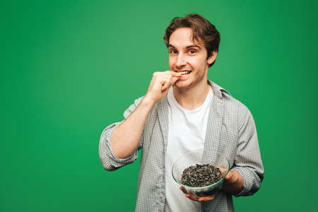 Young man eats sunflower seeds, isolated on green backgroundの写真素材