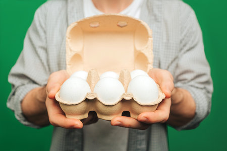 Close up young man holds eggs, isolated on green backgroundの写真素材