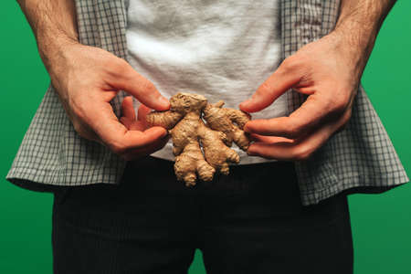 Close up young man holds ginger, isolated on green backgroundの写真素材