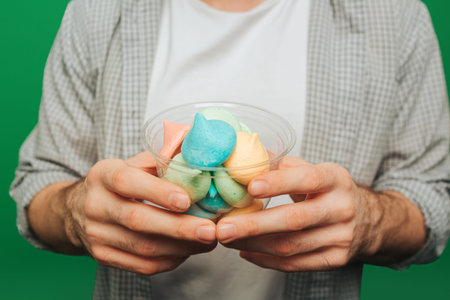 Close up young man holds candies and smile, isolated on green background