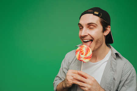 Young man lick lollipop with enjoy, isolated on green backgroundの写真素材