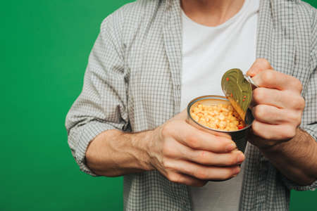 Close up young man opens corn in a jar, isolated on green backgroundの写真素材