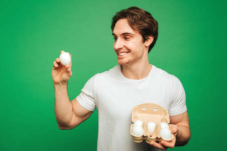 Young man smiles and holds eggs, isolated on green backgroundの写真素材