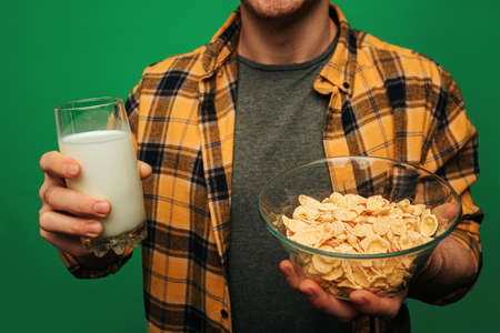 Man holds glass of milk and flakes, isolated on green backgroundの写真素材