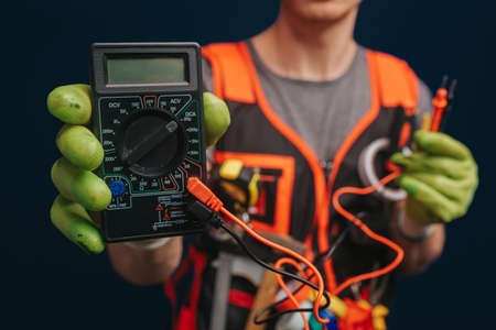 Close up builder is holding digital multimetert in gloves, isolated over blue backgroundの写真素材