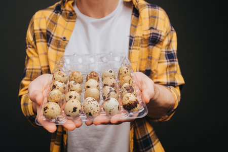 Close up of young blond man in yellow shirt is holding quail egg packing, isolated over black backgroundの写真素材
