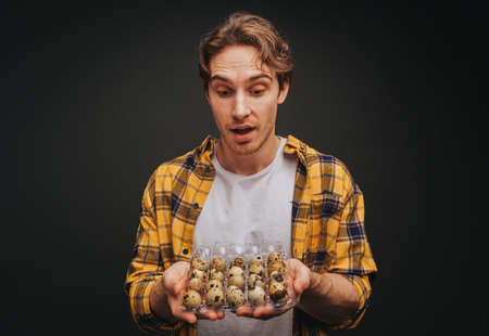 Young blond man in yellow shirt is holding quail egg packing, isolated over black backgroundの写真素材