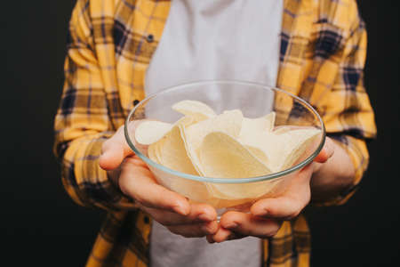 Close up, young blond man in yellow shirt is holding plate with chips, isolated over black backgroundの写真素材