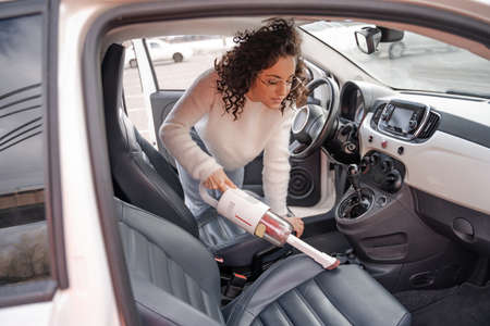 Girl vacuuming car seat with vacuum cleaner in carの写真素材