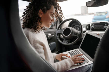 European girl typing laptop computer in automobileの写真素材