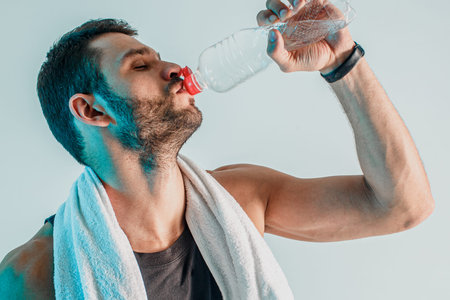 Tired young sportsman drinking water from bottle