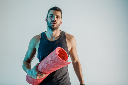 Serious sportsman hold fitness mat in studio