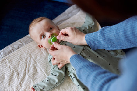 Mother giving pacifier into mouth of newborn baby