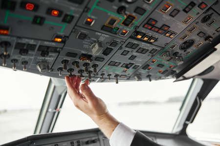 Male pilot turning button on passenger airplaneの写真素材