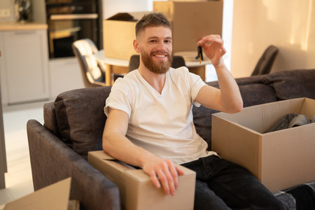Man sitting on sofa and showing key of new homeの写真素材