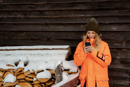 Beautiful girl smiling snowboarder standing alone with phone in hands. Mountain outdoor, winter...