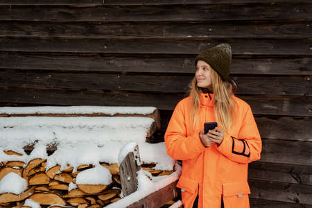 Beautiful girl snowboarder standing alone with phone in hands. Mountain outdoor, winter sport activity.の写真素材