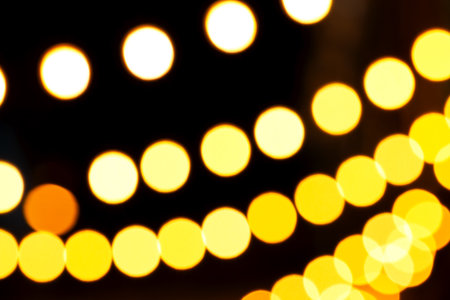 Warm yellow and white bokeh lights forming soft glowing circles against deep black background, creating cozy, atmospheric visual suitable for holiday themes, creative designs, decorative backdropsの写真素材