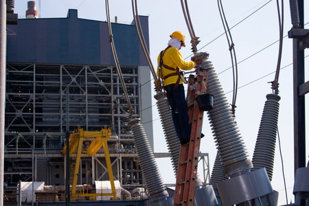 Worker at the switch yard for maintenance work with power plant at the background
