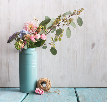 flowers and tree branch in can on blue table, floral composition