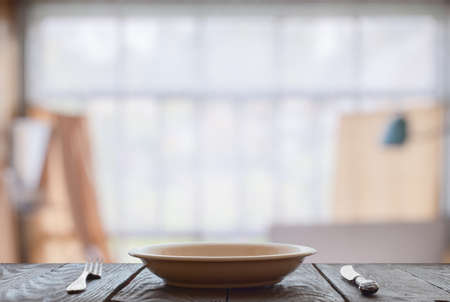 empty plate with fork and knife on wooden table in room with big windowsの写真素材