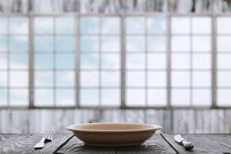empty plate with fork and knife on wooden table in room with big windowsの写真素材