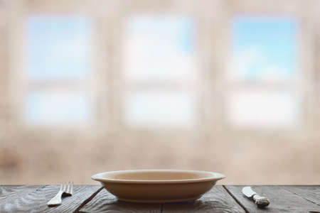 empty plate with fork and knife on wooden table in room with big windowsの写真素材