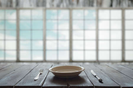 empty plate with fork and knife on old wooden table in room with big windowsの写真素材
