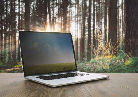 pc on wooden table, sunset forest backgroundの写真素材