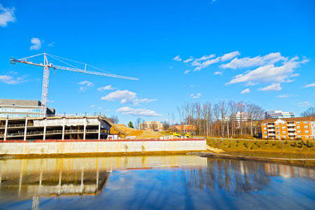 New building construction site near pond  Construction equipment on a clear sunny day with reflections in icy water のeditorial素材