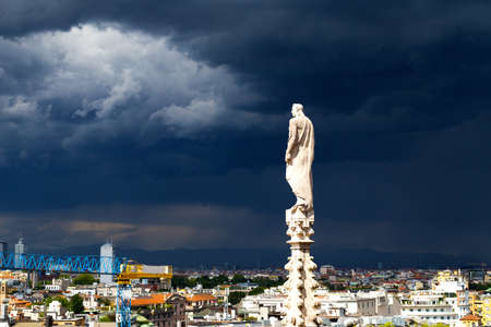 A statue of the Dome of Milan cathedral with the city view before the thunder  Arial view of Milan downtown from height of dome steeple  の写真素材