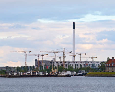 Building Cranes at sunset. Multiple cranes at the construction site of modern buildings near a small sea port in Copenhagen Denmarkの写真素材