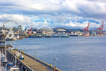 Seattle Great Wheel and port cranes under blue cloudy sky in Seattle downtown. Late afternoon sun touched piers along Alaskan Way in Seattle downtown.のeditorial素材