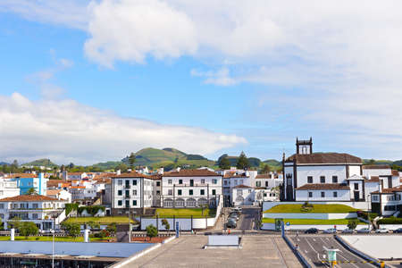 View on Ponta Delgada from the ocean pier, Azores, Portugal. White houses with colorful tiled roofs and countryside with mountain ridge on the horizon.の写真素材