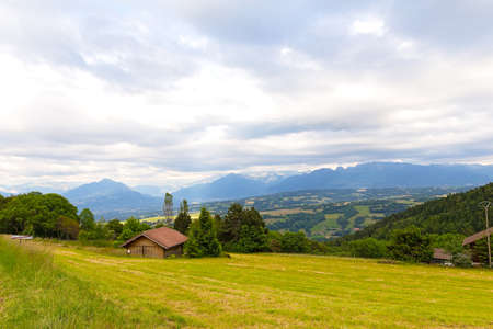 Panoramic view of Swiss Alps near Geneva, Switzerland. Farmhouses and hilly countryside on a cloudy day in summer.の写真素材