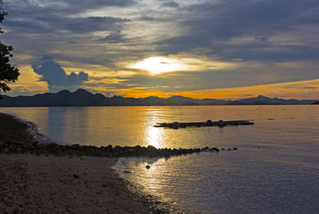 Sunset at the sandy beach with mountain ridge on the horizon, Coron Island, Philippines. Golden sun reflection on a calm sea water at dusk.の写真素材