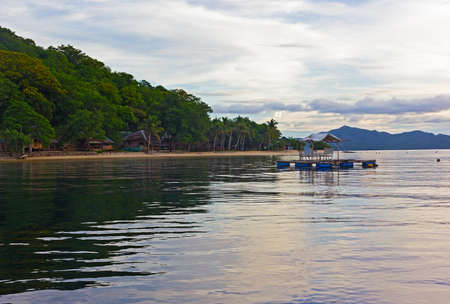 Beach on a small island with floating gazebo in sea waters. Quiet sea at dawn on a tropical beach in Philippines.の写真素材